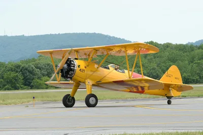 A classic yellow Boeing Stearman biplane on the tarmac at an airport