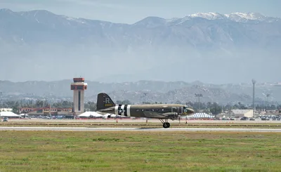 A historic Douglas C-47 Skytrain warbird on a ramp with the snow-capped San Bernardino Mountains in the background.