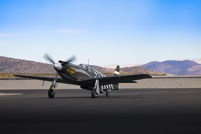 Vintage P-51 Mustang aircraft on a desert runway with mountains in the background