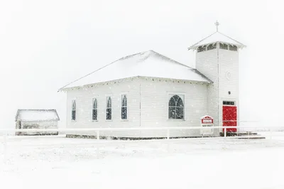 A serene winter scene of a white country church surrounded by snow in Eureka, Kansas.