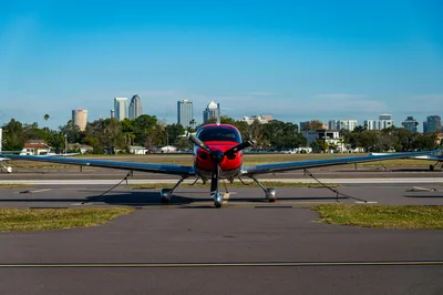 A small aircraft parked on a tarmac with a city skyline in the background under a clear blue sky.